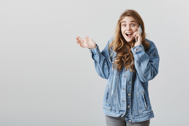 La niña feliz emocionada recibe buenas noticias a través de una llamada telefónica, hablando por teléfono inteligente