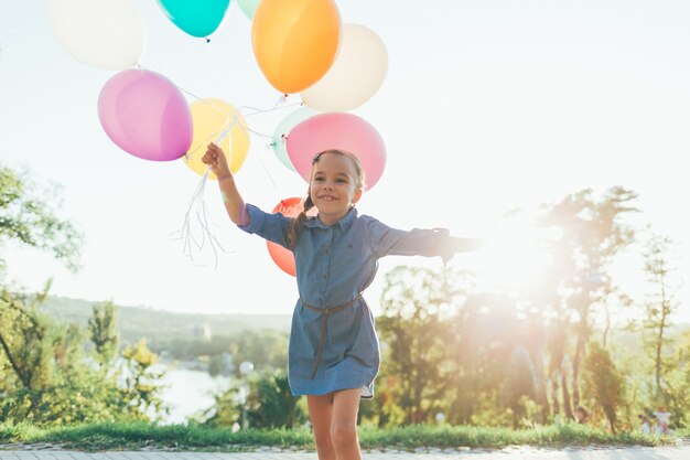 Niña feliz con globos de colores en el parque de la ciudad