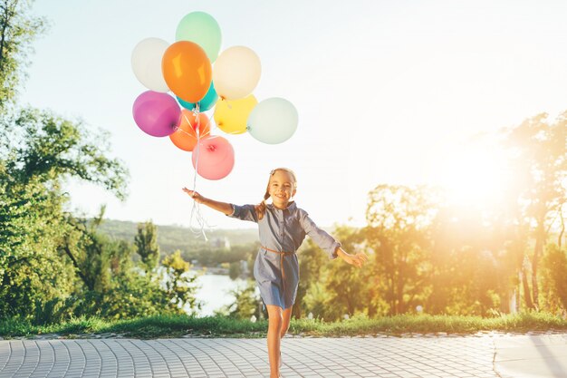 Niña feliz con globos de colores en el parque de la ciudad