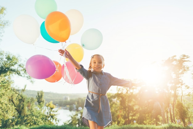 Niña feliz con globos de colores en el parque de la ciudad