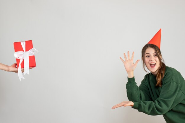 Niña feliz con gorro de fiesta abriendo sus manos apuntando a la mano humana sosteniendo un regalo en blanco