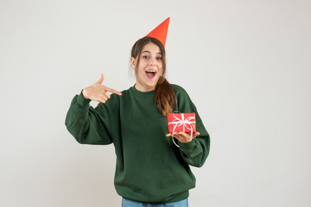 Niña feliz con gorro de fiesta apuntando a su regalo en blanco