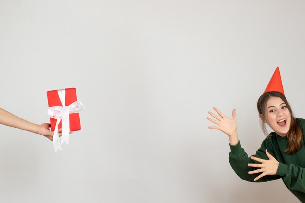 Niña feliz con gorro de fiesta mostrando regalo en mano humana sobre blanco