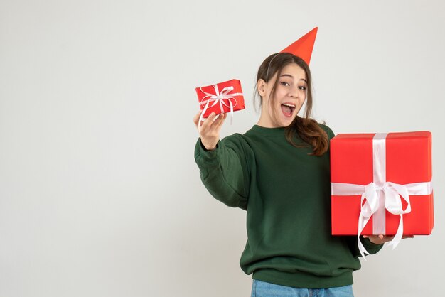 Niña feliz con gorro de fiesta mostrando sus regalos de Navidad en blanco