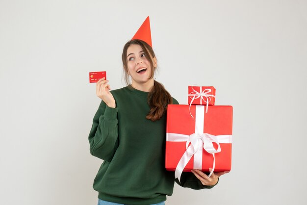 niña feliz con gorro de fiesta sosteniendo regalos y tarjeta en blanco