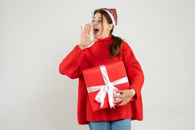 niña feliz con gorro de Papá Noel con regalo llamando a alguien en blanco