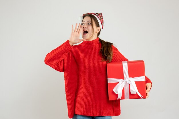 niña feliz con gorro de Papá Noel sosteniendo presente llamando a alguien de pie en blanco