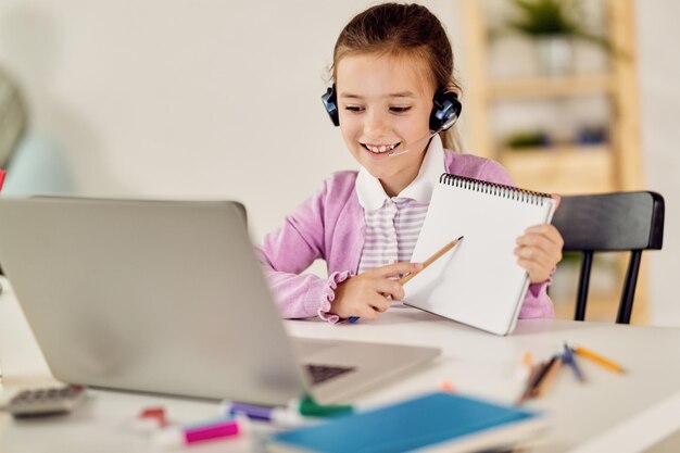 Niña feliz haciendo videollamadas mientras tiene una clase en línea en una computadora portátil