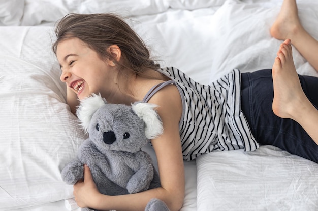 Niña feliz con koala de peluche en la cama