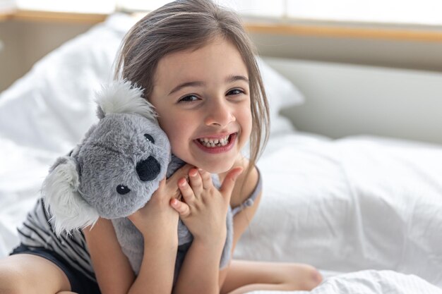 Niña feliz con koala de peluche en la cama