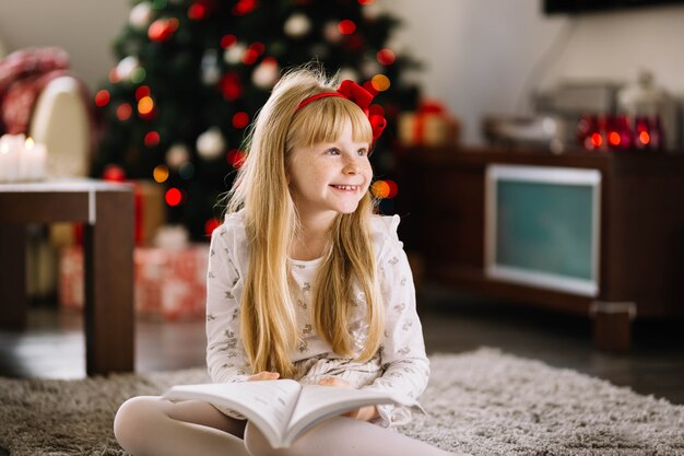 Niña feliz con libro enfrente de árbol de navidad