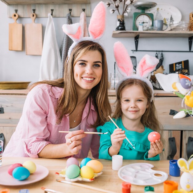 Niña feliz con madre pintando huevos para pascua