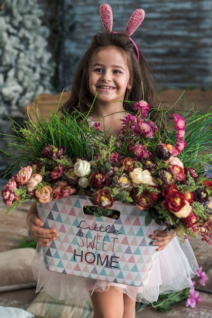 Niña feliz en orejas de conejo con flores en bolsa