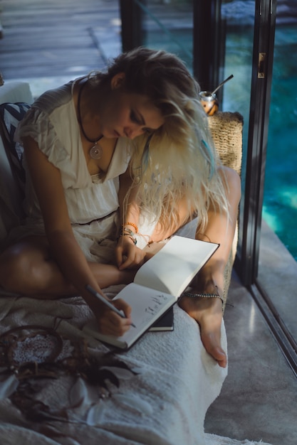 niña feliz pasa tiempo en casa en un interior acogedor, escribe y dibuja en un cuaderno.