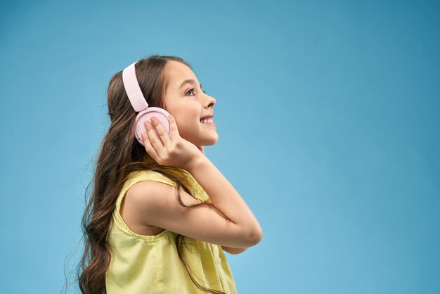 Niña feliz con el pelo largo en auriculares rosa sonriendo.