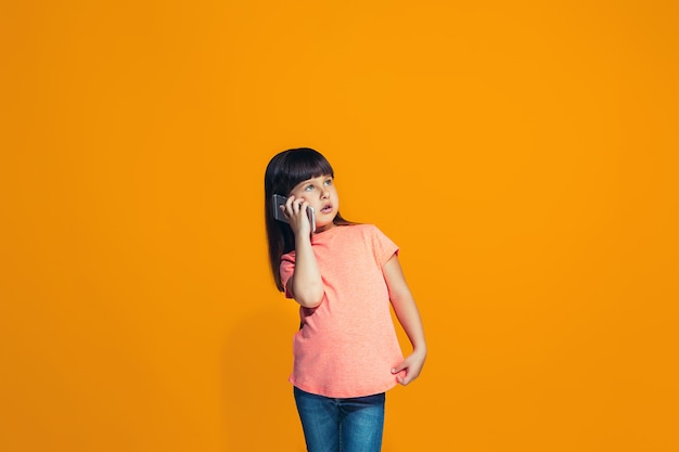 La niña feliz de pie y sonriendo contra la pared naranja