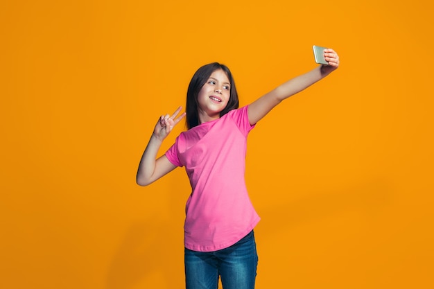 La niña feliz de pie y sonriendo contra la pared naranja