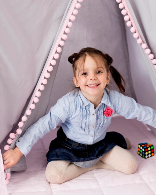 Niña feliz posando en tienda de campaña en casa