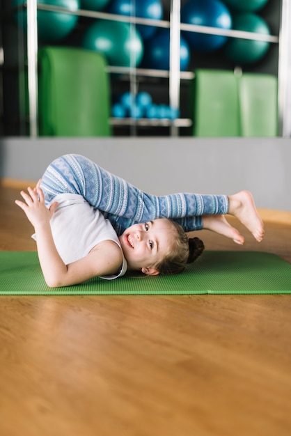 Foto gratuita niña feliz practicando yoga en la estera mirando a la cámara