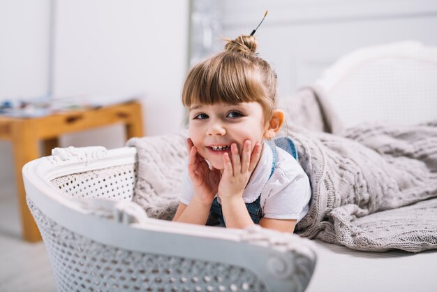 Niña feliz que miente en el sofá debajo de la manta