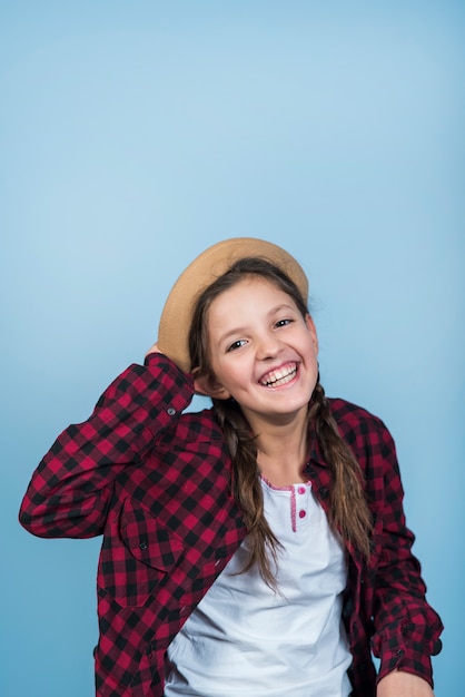 Niña feliz que sostiene el sombrero en la cabeza