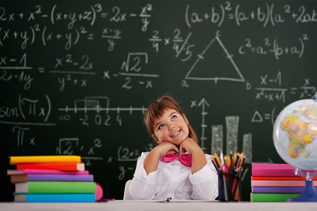 Niña feliz sentada y soñando en el aula