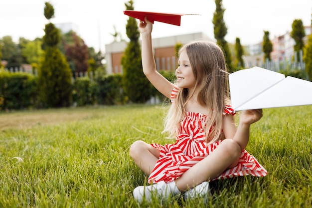 niña feliz sonriente con aviones de papel al aire libre