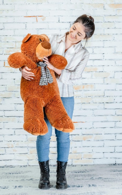 Niña feliz sonriente sosteniendo un oso de peluche y mirándolo Foto de alta calidad