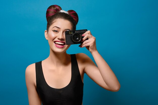 Niña feliz sonriente tomando fotos con una cámara vieja