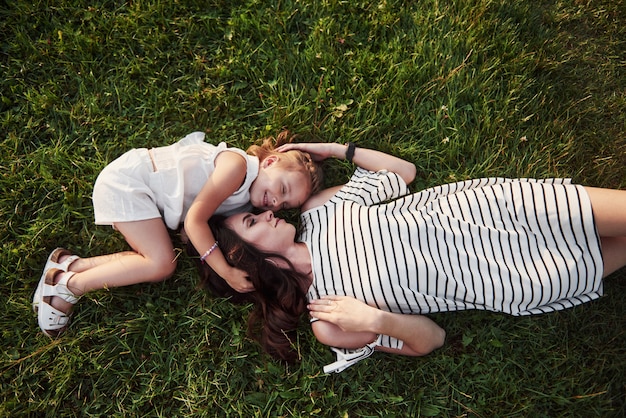 Niña feliz y su madre que se divierten al aire libre en la hierba verde en día soleado de verano.