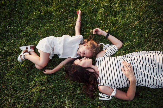 Niña feliz y su madre que se divierten al aire libre en la hierba verde en día soleado de verano.