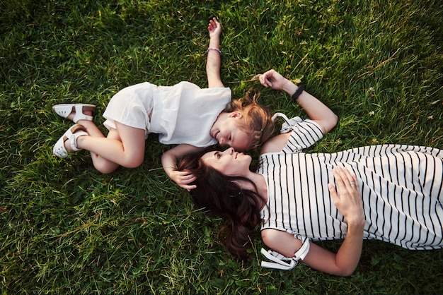 Niña feliz y su madre que se divierten al aire libre en la hierba verde en día soleado de verano.