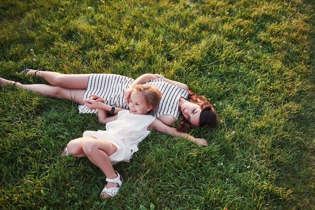 Niña feliz y su madre que se divierten al aire libre en la hierba verde en día soleado de verano.