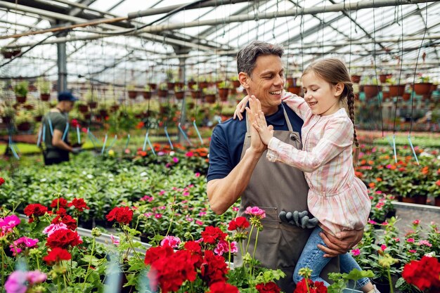 Una niña feliz y su padre chocan los cinco mientras están en un invernadero y cuidan las flores