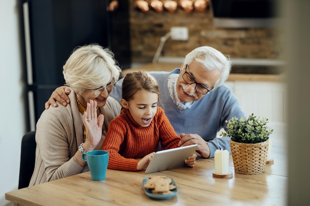 Niña feliz y sus abuelos usando el panel táctil y haciendo videollamadas en casa