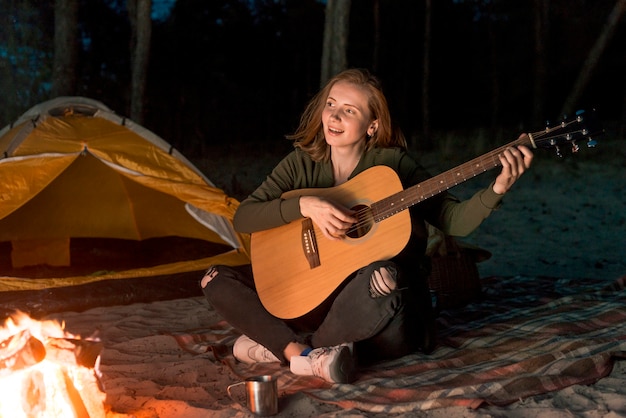 Niña feliz tocando la guitarra junto a una hoguera