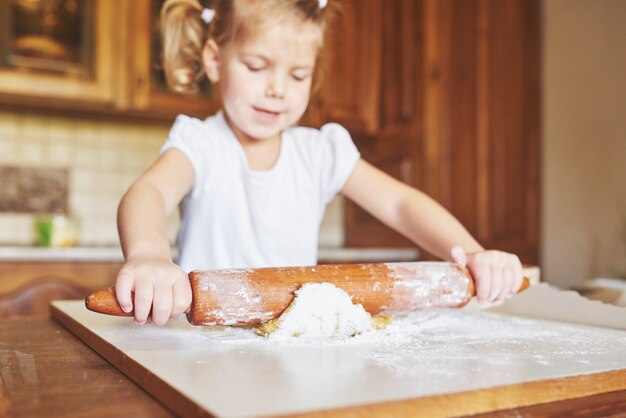 Una niña feliz usa una masa. Bebé hacer la cena en traje de chef