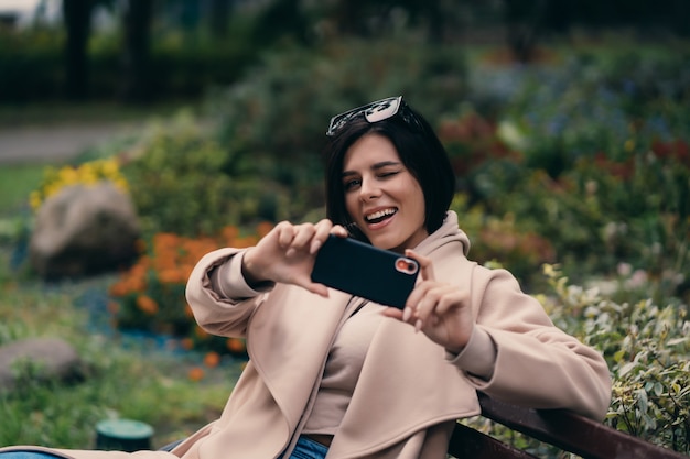 Niña feliz usando un teléfono inteligente en un parque de la ciudad sentado en un banco