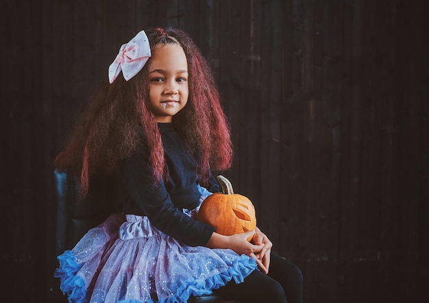 Foto gratuita niña feliz con vestido festivo posa para el fotógrafo mientras entrega calabaza tallada.