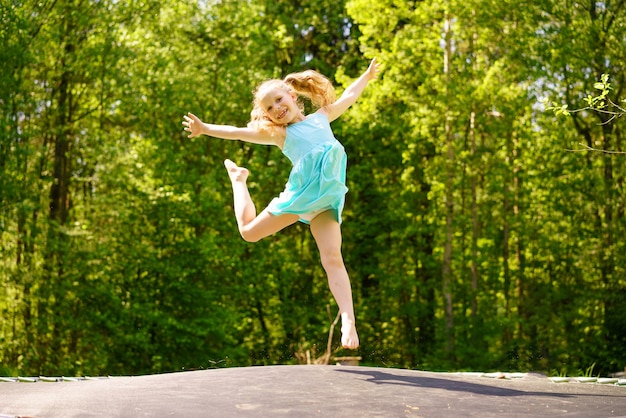 Una niña feliz con un vestido salta sobre un trampolín en un parque en un día soleado de verano