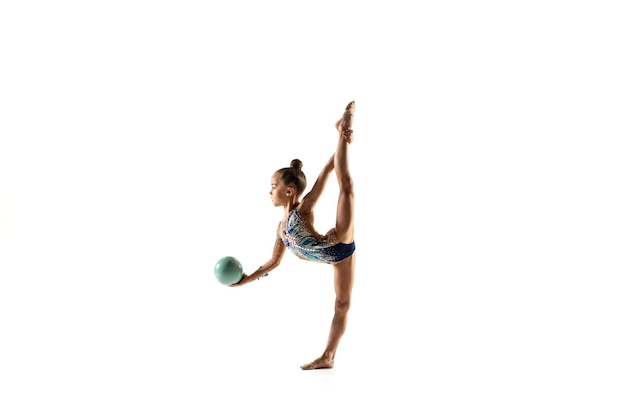 Niña flexible aislada en la pared blanca. pequeña modelo femenina como  artista de gimnasia rítmica en leotardo brillante. gracia en movimiento,  acción y deporte. haciendo ejercicios con la pelota.