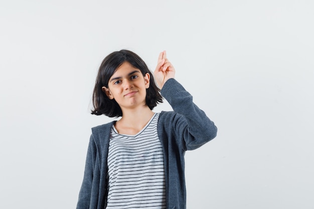 Niña gesticulando con la mano y dos dedos en camiseta, chaqueta y buscando confianza.