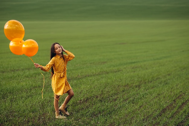 Niña con globos amarillos en el campo.