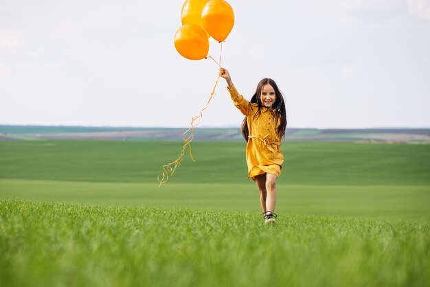 Niña con globos amarillos en el campo.