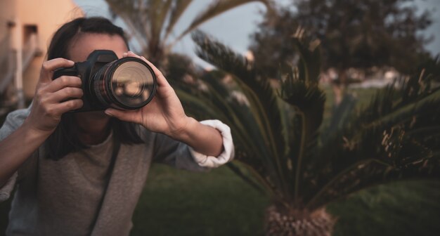 La niña hace una foto con una cámara SLR profesional al aire libre en la naturaleza de cerca.