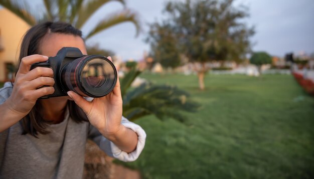 La niña hace una foto con una cámara SLR profesional al aire libre en la naturaleza de cerca.