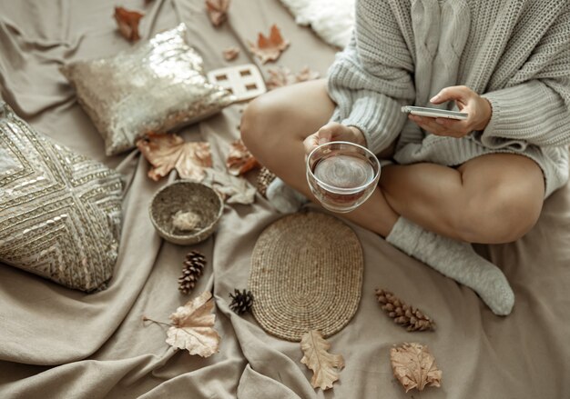 La niña hace una foto de una taza de té entre las hojas de otoño, composición otoñal.