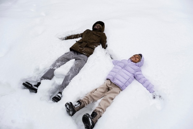 Niña haciendo ángeles de nieve con su padre en invierno