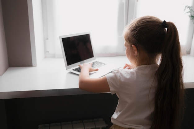 Niña haciendo los deberes en casa con laptop y notebook