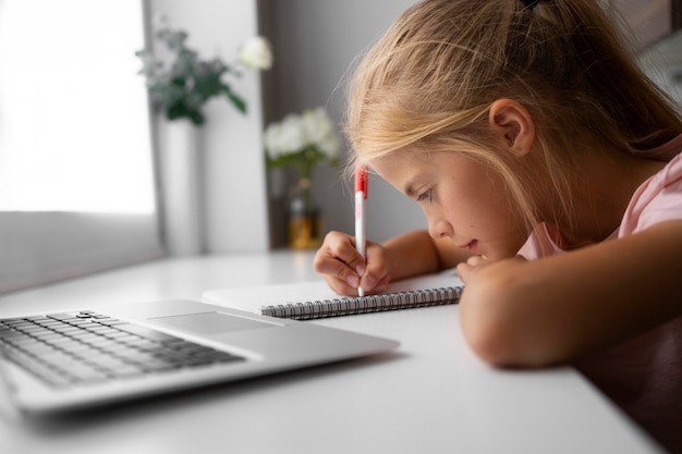 Niña haciendo los deberes en casa con laptop y notebook